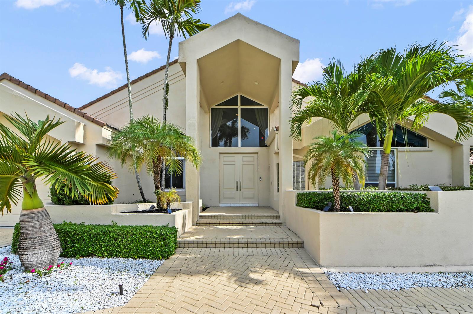 A beige house exterior features a peaked entryway, double front doors, and palm trees — 7165 Mariana Court, Boca Raton FL 33433, BOCA RATON, FL