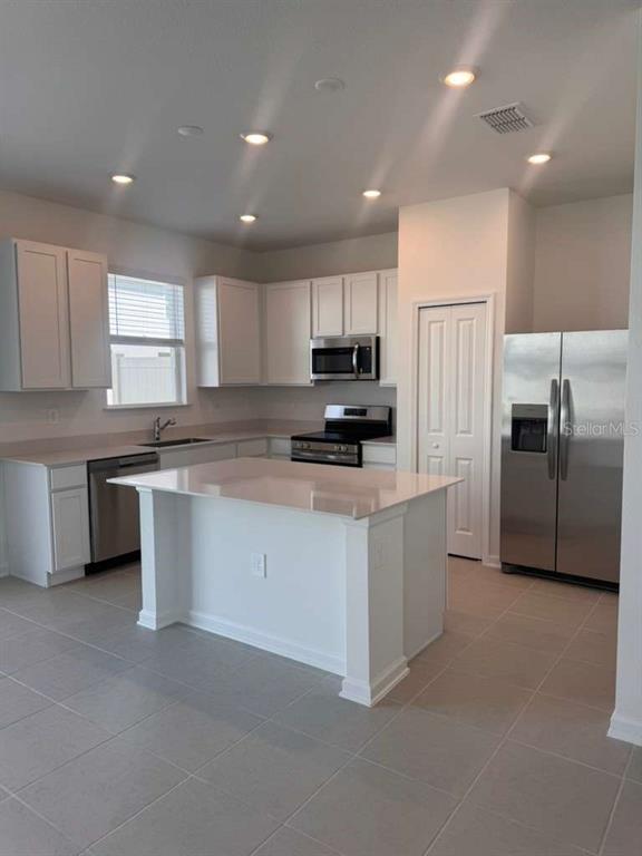 A modern kitchen features white cabinets, stainless steel appliances, and a central island — 3060 CHROMATIC STREET, KISSIMMEE, FL