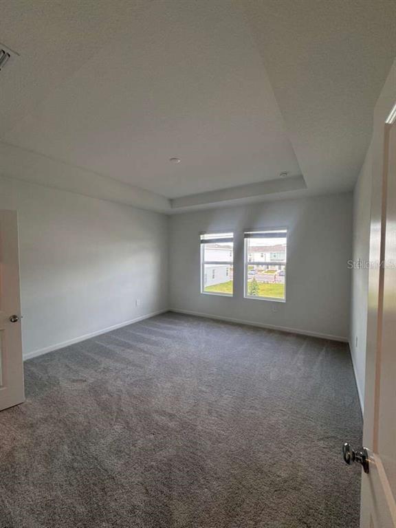 An empty bedroom features gray carpet, white walls, and a tray ceiling — 3060 CHROMATIC STREET, KISSIMMEE, FL