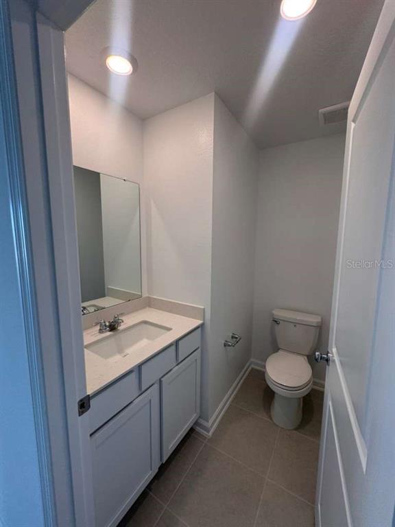 A small bathroom features a white vanity with a sink, a mirror, and a toilet — 3060 CHROMATIC STREET, KISSIMMEE, FL