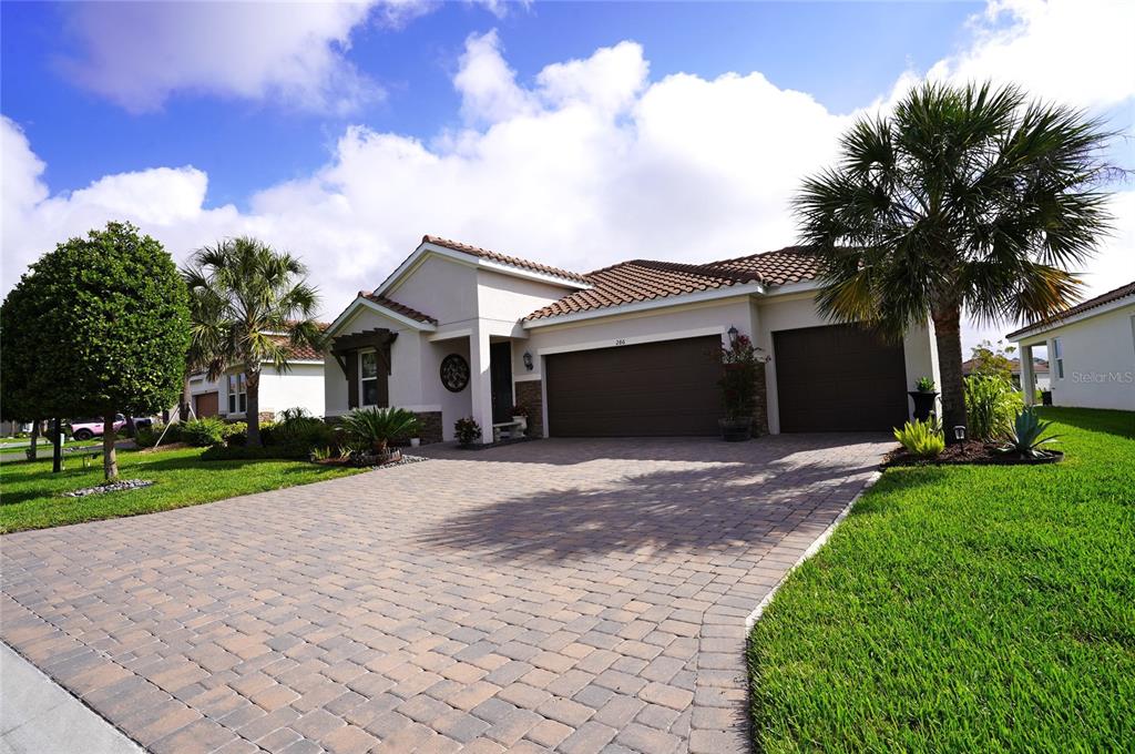 A single-story house with a paved driveway, three-car garage, and palm trees under a sky — 286 DAYLILY BOULEVARD, NOKOMIS, FL