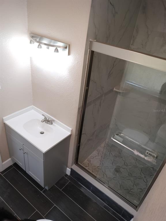 A bathroom features a gray vanity, a walk-in shower with patterned tile, and dark flooring — 3246 NE 7TH LANE, OCALA, FL