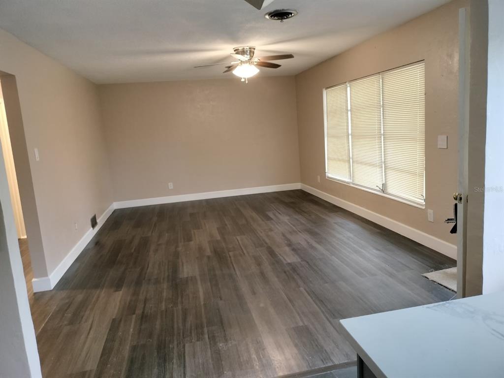 An empty living room features wood-look flooring, beige walls, a ceiling fan, and large windows — 3246 NE 7TH LANE, OCALA, FL