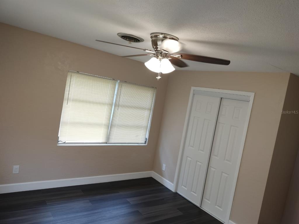 A bedroom with dark wood-look flooring, beige walls, a ceiling fan, and white closet doors — 3246 NE 7TH LANE, OCALA, FL
