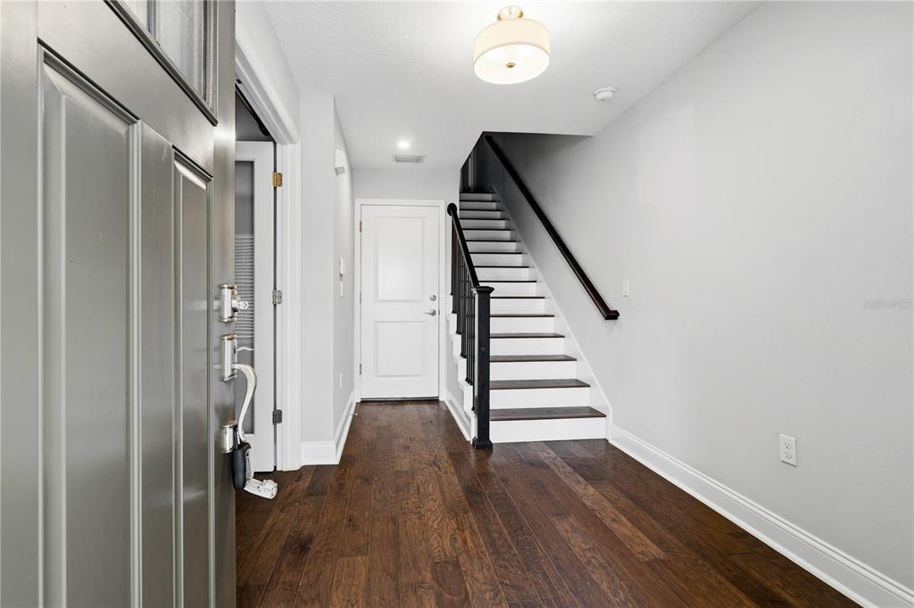An entryway features dark hardwood floors, a white staircase with a black railing, and a door — 858 N THORNTON AVENUE, ORLANDO, FL