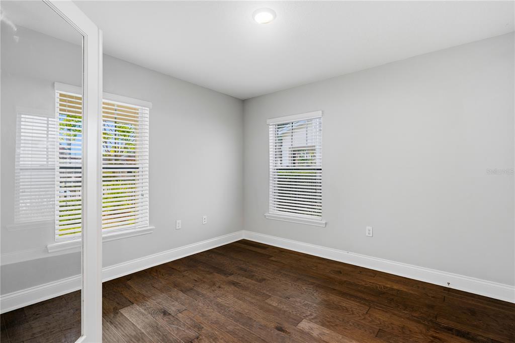 An empty bedroom features light gray walls, dark wood flooring, and two windows with blinds — 858 N THORNTON AVENUE, ORLANDO, FL