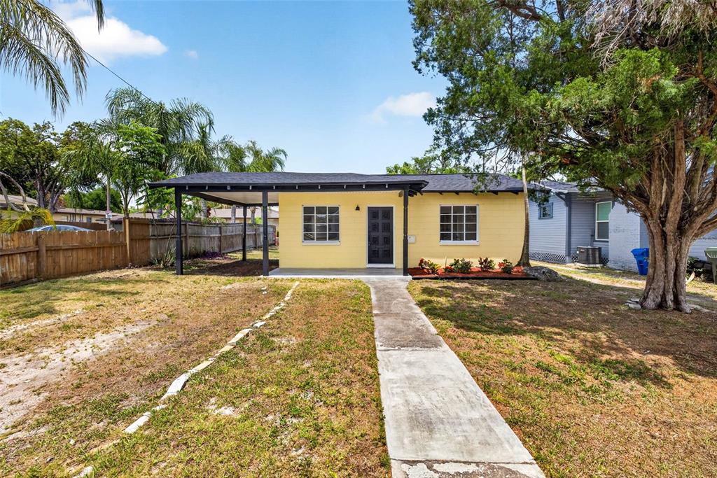 A yellow single-story house features a front porch, a concrete walkway, and a large tree — 834 E LIME STREET, LAKELAND, FL