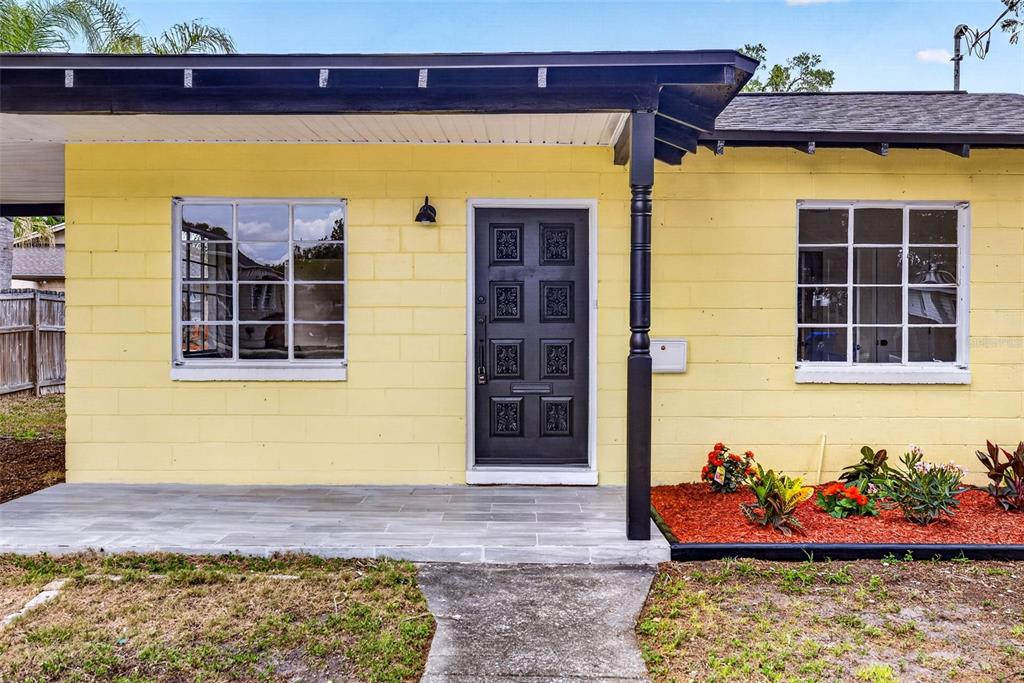 A yellow concrete block house features a black front door and a tiled front porch — 834 E LIME STREET, LAKELAND, FL