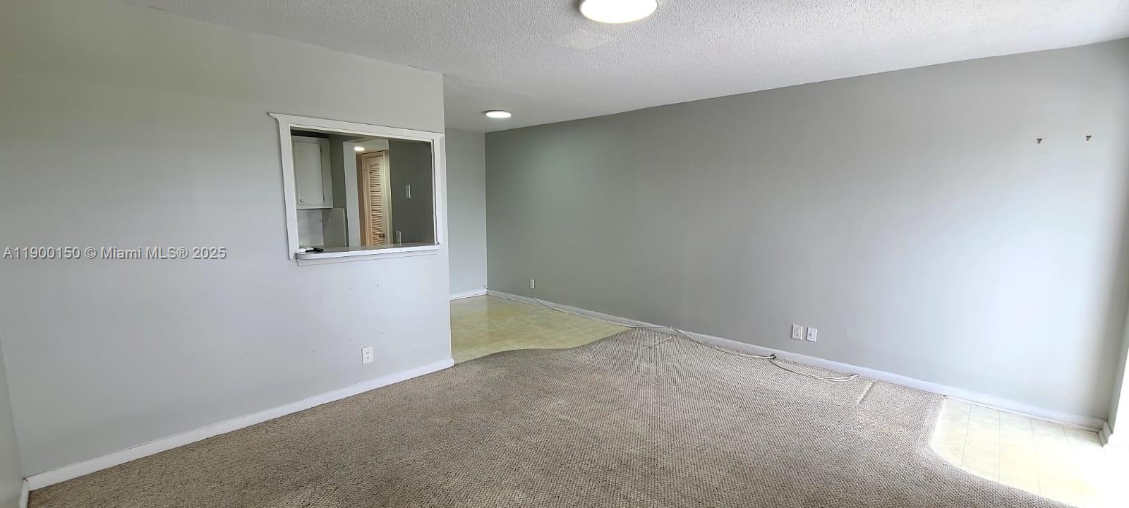 An interior view shows a carpeted living area with a pass-through window to a kitchen — 92 Berkshire D # 92, West Palm Beach FL 33417, WEST PALM BEACH, FL