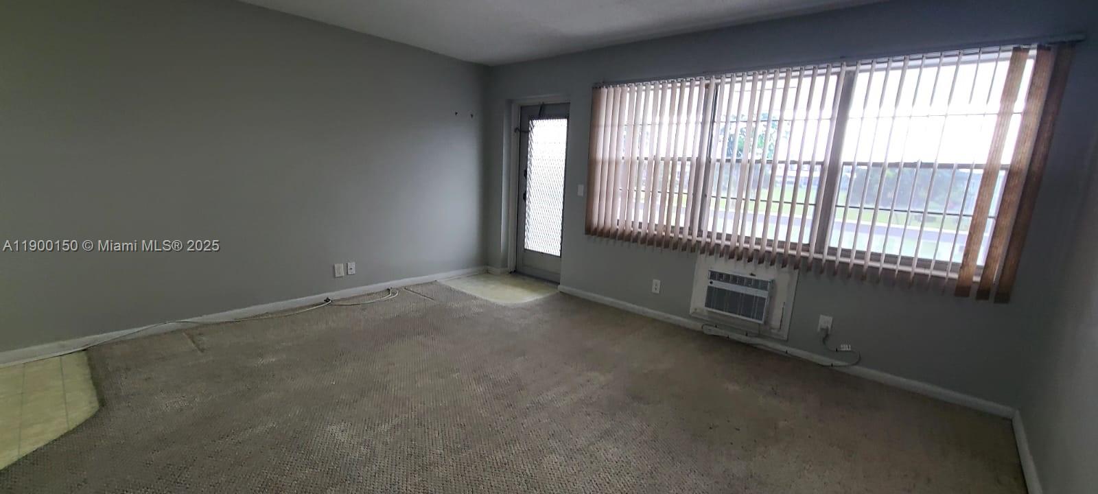 An empty room features beige carpeting, gray walls, vertical blinds, and a window air conditioner — 92 Berkshire D # 92, West Palm Beach FL 33417, WEST PALM BEACH, FL