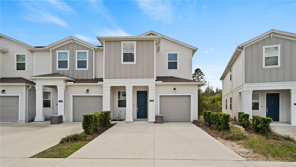 A two-story townhouse exterior features light siding, a gray garage, and a blue front door — 7428 STONE CREEK TRAIL, KISSIMMEE, FL