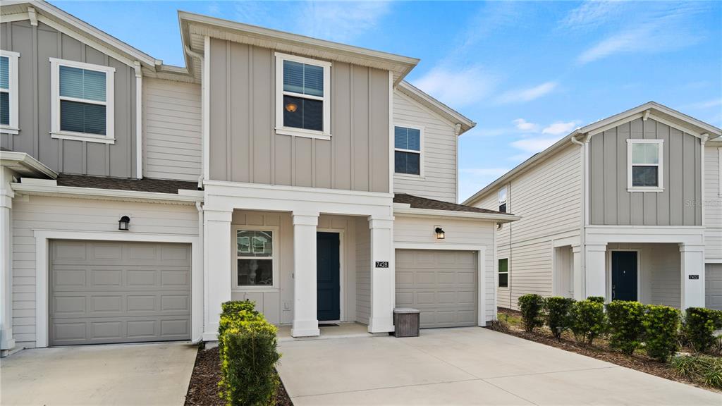 The exterior of two adjacent two-story townhomes features light siding, garages, and small front landscaping — 7428 STONE CREEK TRAIL, KISSIMMEE, FL