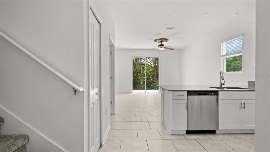 A kitchen with white cabinets and stainless steel appliances overlooks a living area with tile — 7428 STONE CREEK TRAIL, KISSIMMEE, FL