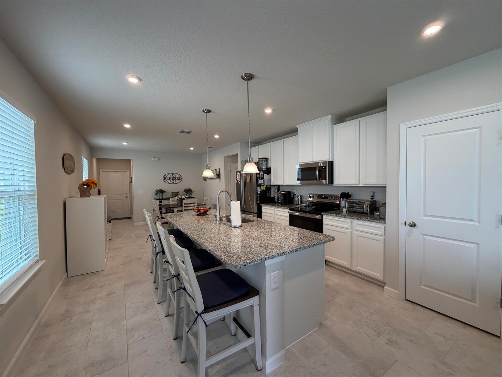 A kitchen features white cabinets, granite countertops, a central island with seating, and tile flooring — 3030 Ruby Fls Drive, Deland FL 32724, DELAND, FL