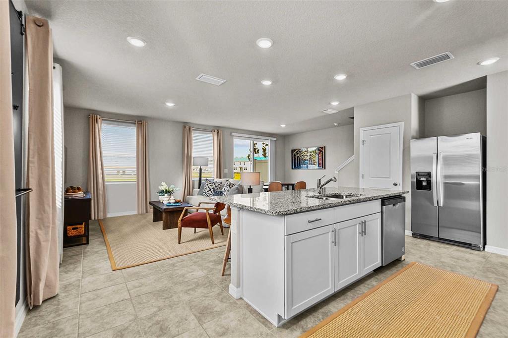 A kitchen with a granite island and stainless steel refrigerator overlooks a living room area — 8683 HOLLY GROVE COURT UNIT Calistoga, RIVERVIEW, FL