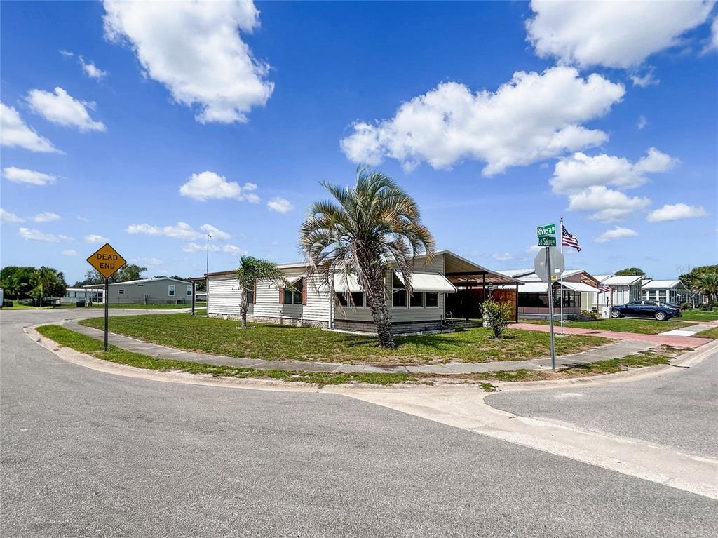 A single-story mobile home sits on a corner lot with a palm tree and street signs — 36412 LE SABRE WAY, ZEPHYRHILLS, FL