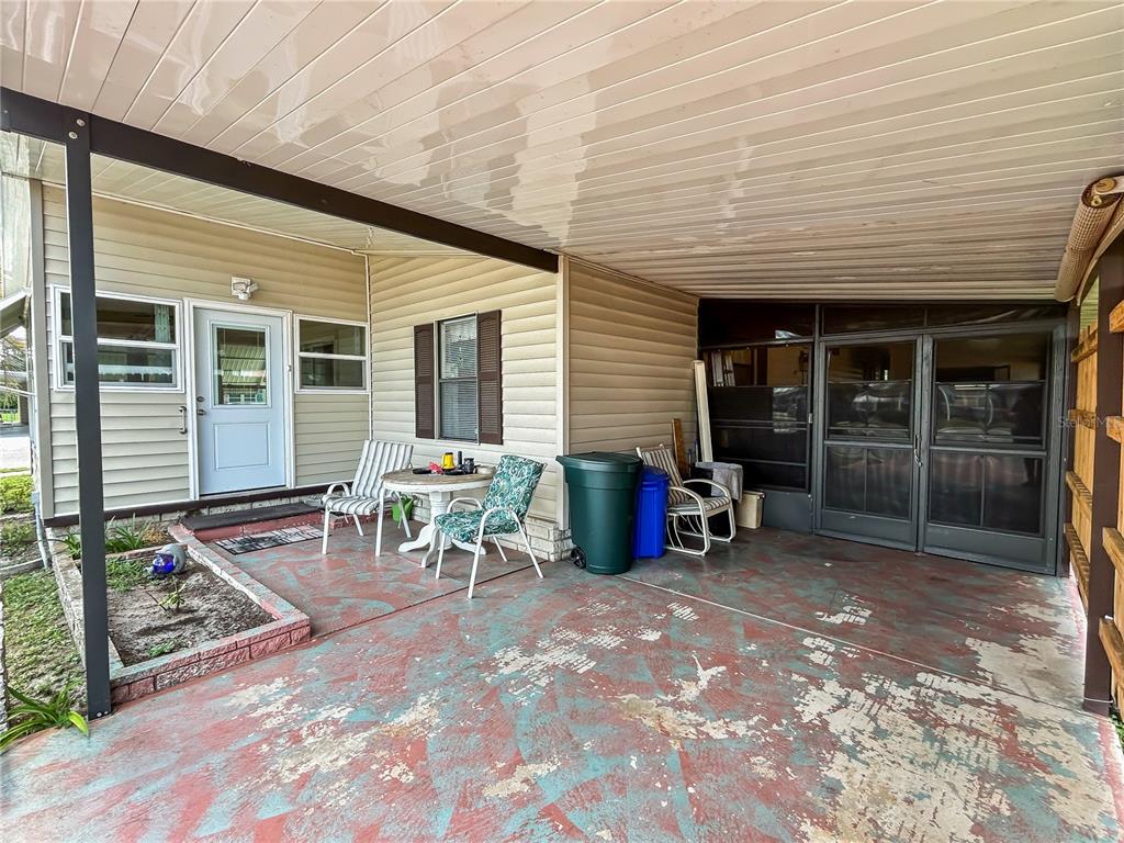 A covered carport features a painted concrete floor, outdoor seating, and a screened-in porch entrance — 36412 LE SABRE WAY, ZEPHYRHILLS, FL