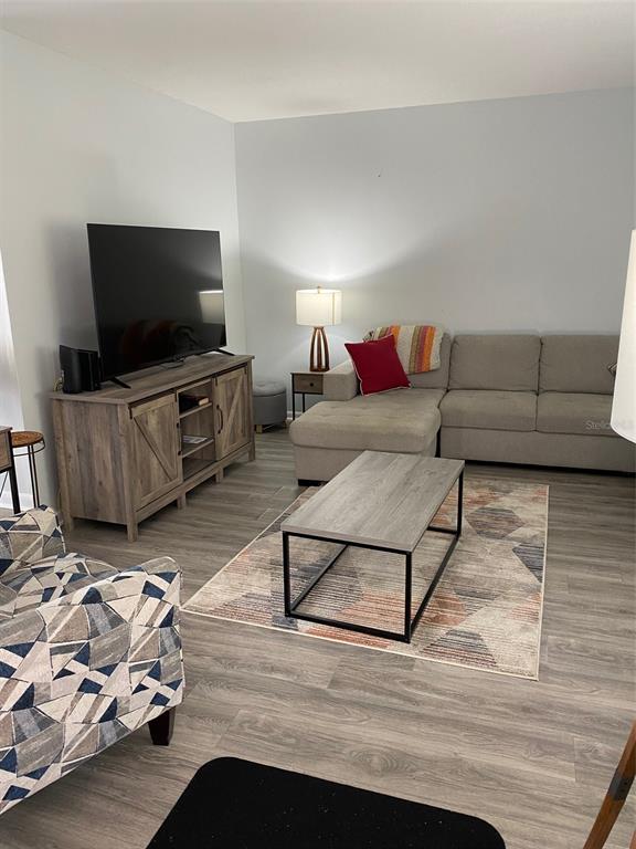 A living room features a gray sectional sofa, a television console, and a geometric rug — 2209 BELLEAIR ROAD UNIT C21, CLEARWATER, FL