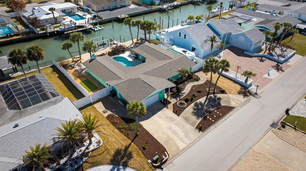 An aerial view shows a waterfront house with a pool, putting green, and paved driveway — 119 OLD CARRIAGE ROAD, PONCE INLET, FL