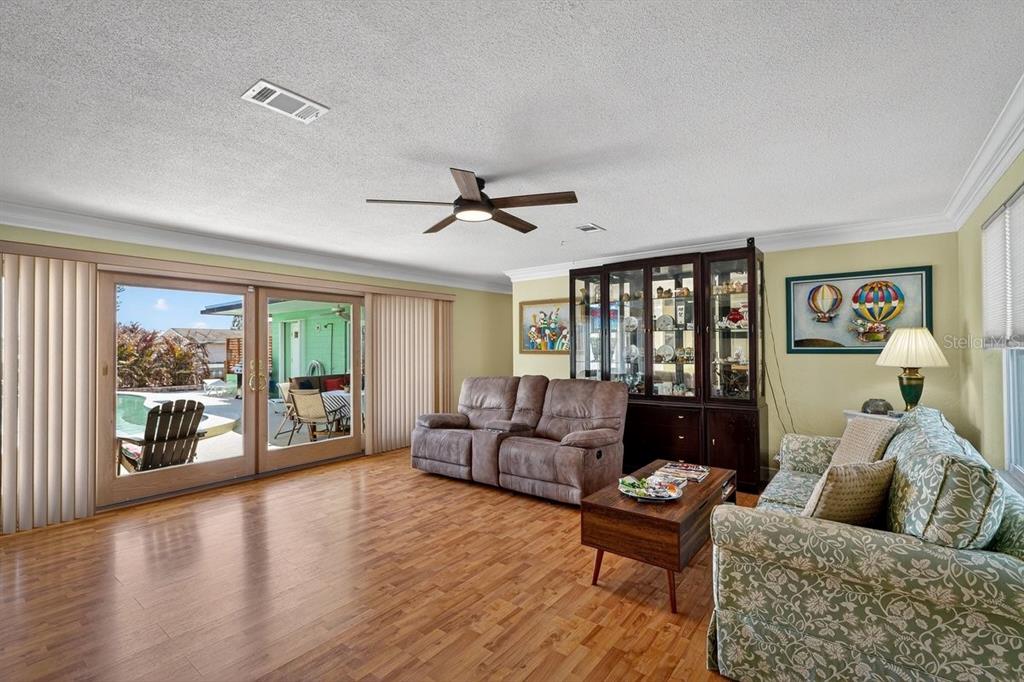 A living room with wood flooring, a ceiling fan, a sofa, and sliding glass doors — 119 OLD CARRIAGE ROAD, PONCE INLET, FL