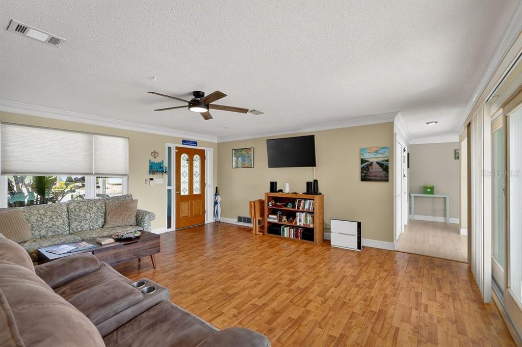 A living room with wood flooring, a ceiling fan, a television, and a wooden front door — 119 OLD CARRIAGE ROAD, PONCE INLET, FL