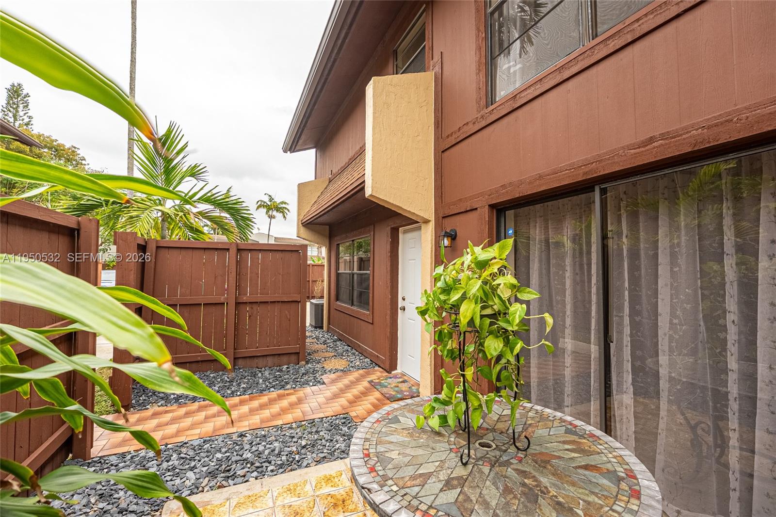 A brown two-story building exterior features a tiled walkway, a small patio, and landscaping — 6534 SW 114th Pl # 75, Miami FL 33173, MIAMI, FL
