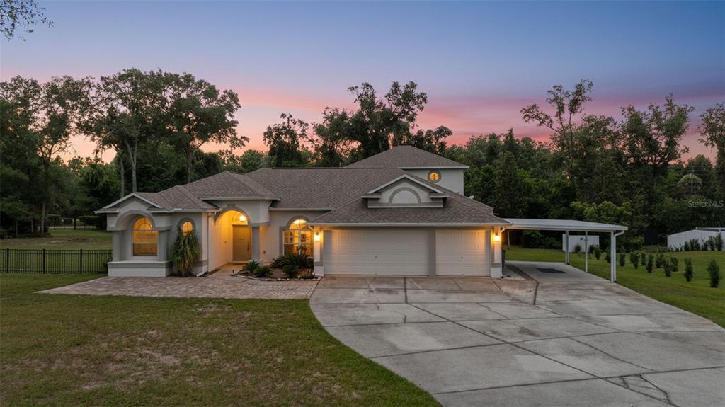 A single-story house with a two-car garage, attached carport, and arched windows at sunset — 13123 SADDLE WAY, BROOKSVILLE, FL