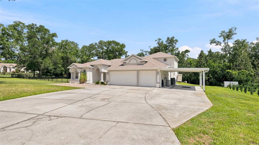A light-colored house with a two-car garage and a side carport sits on a lot — 13123 SADDLE WAY, BROOKSVILLE, FL