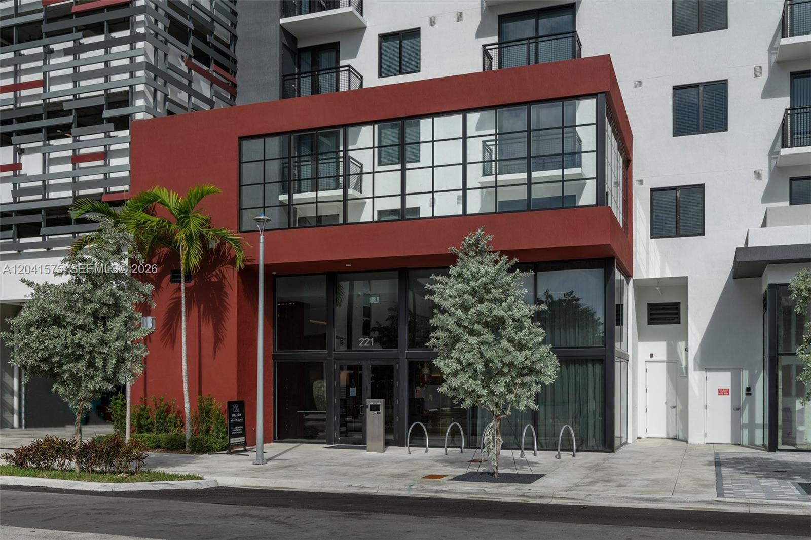 The exterior of a modern building features a red facade, large windows, and palm trees — 221 SW 12th St # 511, Miami FL 33130, MIAMI, FL