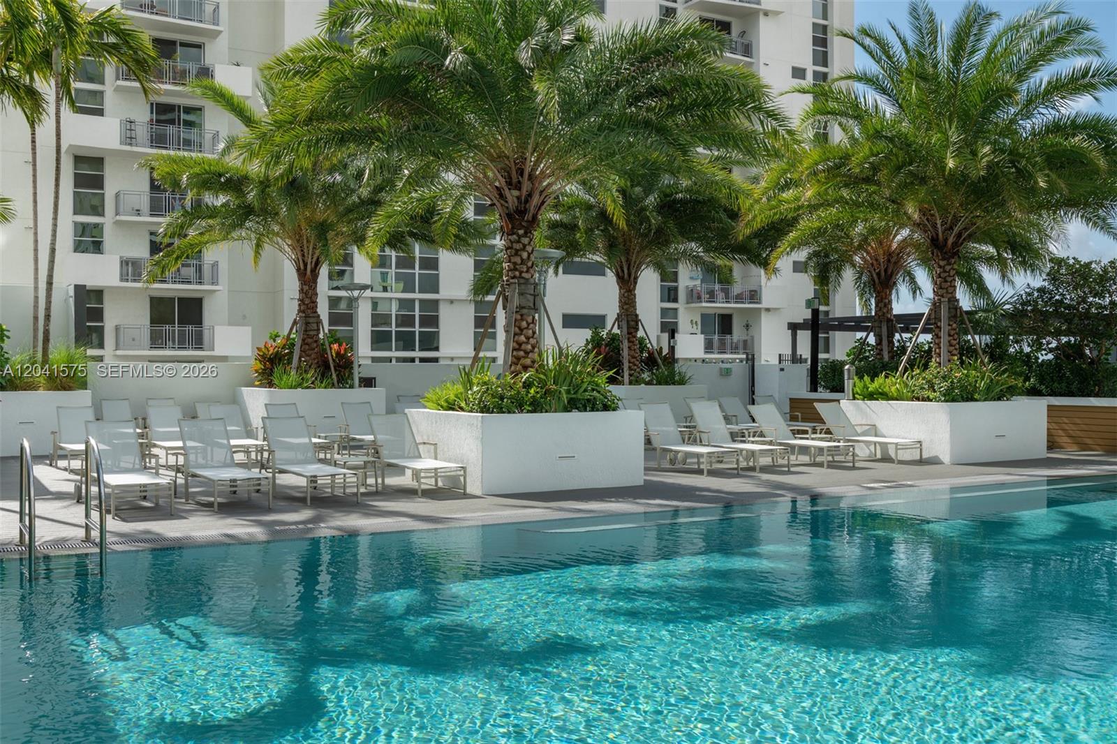 A swimming pool with lounge chairs and palm trees in front of a residential building — 221 SW 12th St # 511, Miami FL 33130, MIAMI, FL