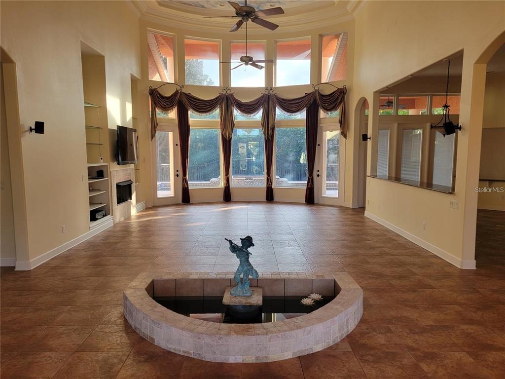 A spacious living room features a central indoor fountain, tile flooring, and tall arched windows — 10209 THURSTON GROVES BOULEVARD, LARGO, FL