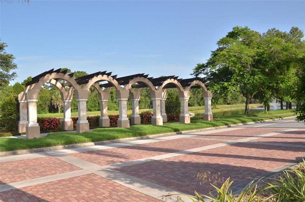 A brick driveway leads past a series of stone arches with wooden trellises near a pond — 5121 GLADE FERN COURT, SARASOTA, FL