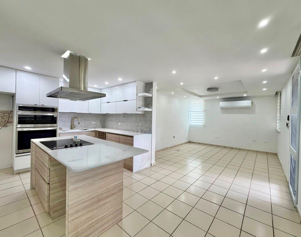 A modern kitchen features white cabinetry, a wood-toned island with a cooktop, and tiled floors — Calle 5 PARQUE SAN MIGUEL UNIT H-8, BAYAMON, PR
