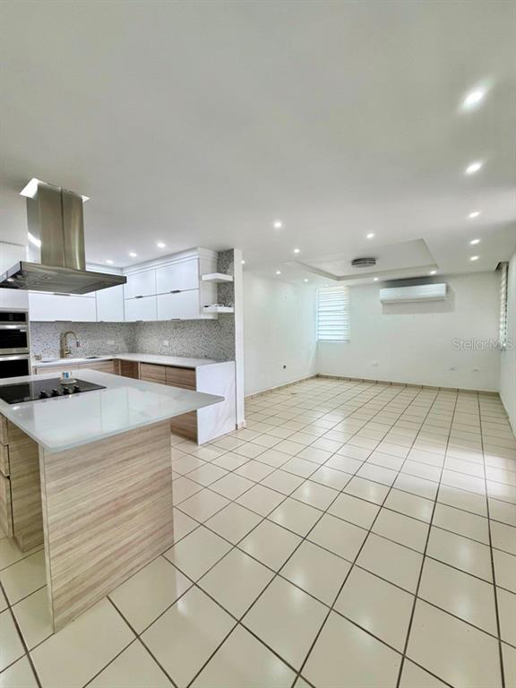 A modern kitchen with a white island and light wood cabinetry opens to a tiled room — Calle 5 PARQUE SAN MIGUEL UNIT H-8, BAYAMON, PR