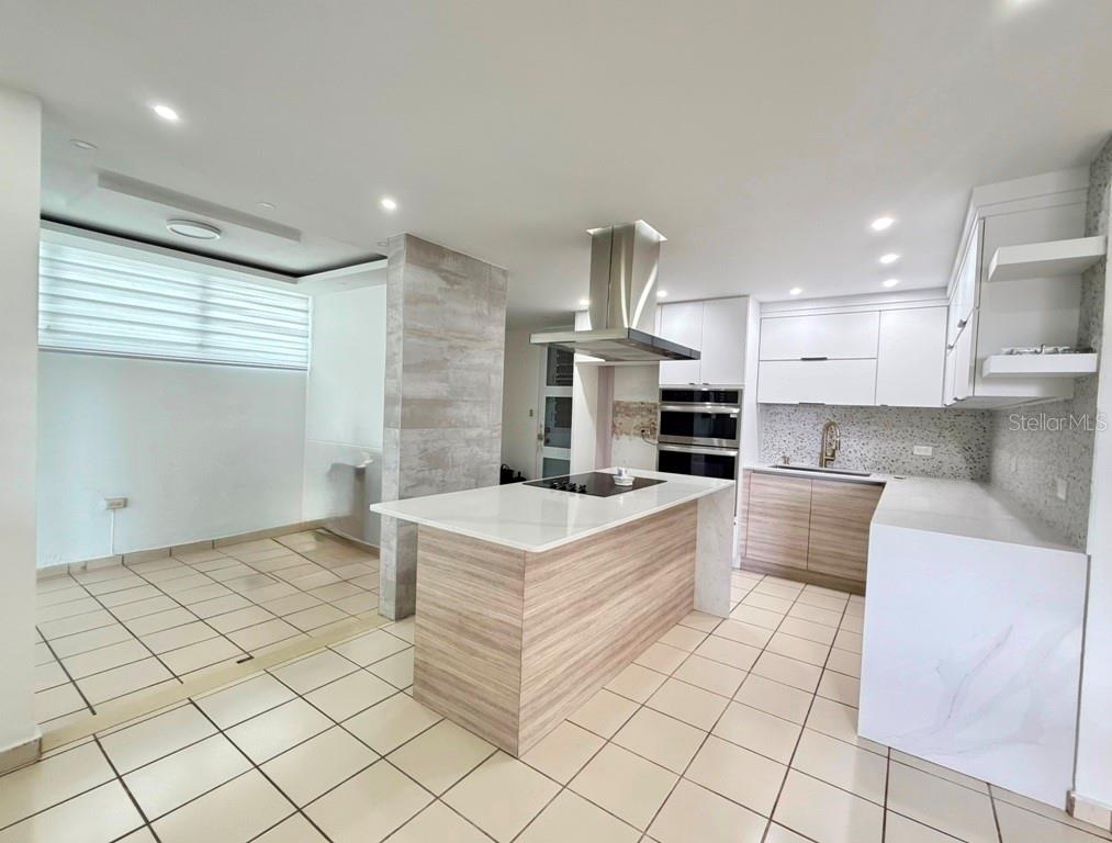 A modern kitchen features white cabinetry, a wood-toned island with a cooktop, and tile flooring — Calle 5 PARQUE SAN MIGUEL UNIT H-8, BAYAMON, PR
