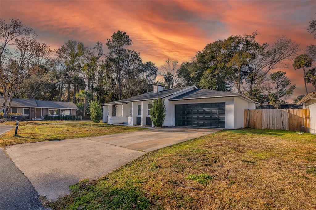A white single-story house with a dark garage door and a concrete driveway at sunset — 872 FALKIRK DRIVE, WINTER SPRINGS, FL