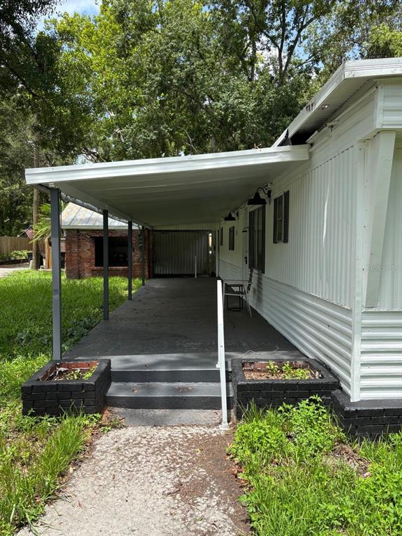 A covered concrete patio area sits beside a white mobile home with black brick planters — 24739 AUDREY ROAD, LAND O LAKES, FL