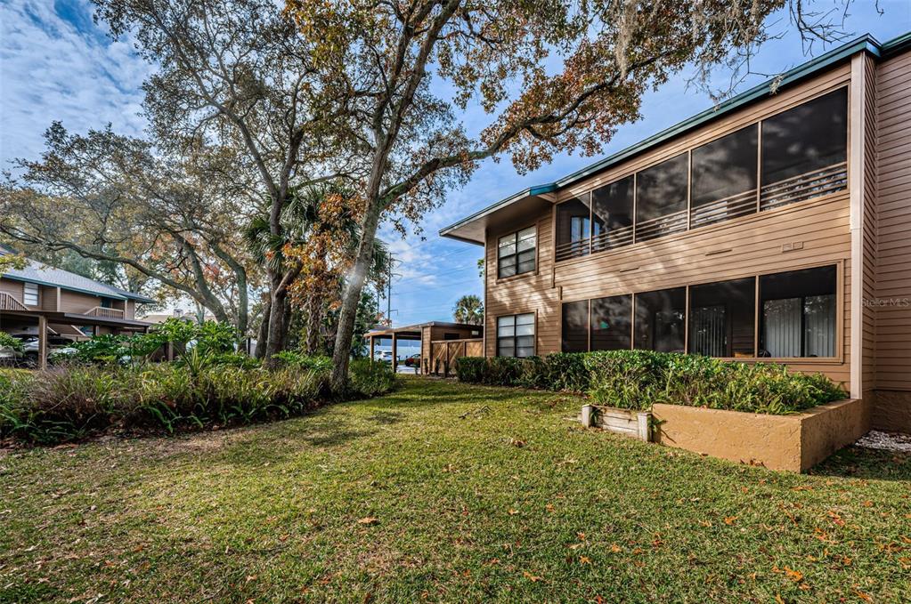 The exterior of a two-story tan building features screened-in porches and a grassy yard — 802 LENNOX ROAD W UNIT 802, PALM HARBOR, FL