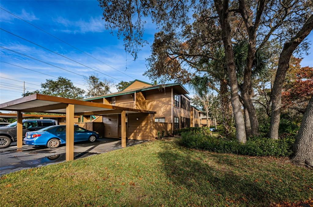 A two-story brown building with a covered carport and a blue sedan parked underneath — 802 LENNOX ROAD W UNIT 802, PALM HARBOR, FL