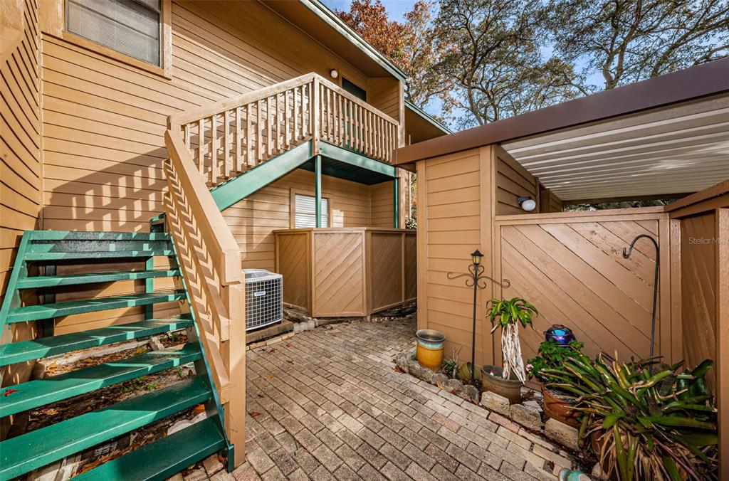 A brick patio features an outdoor staircase leading to a second-story balcony and a carport — 802 LENNOX ROAD W UNIT 802, PALM HARBOR, FL