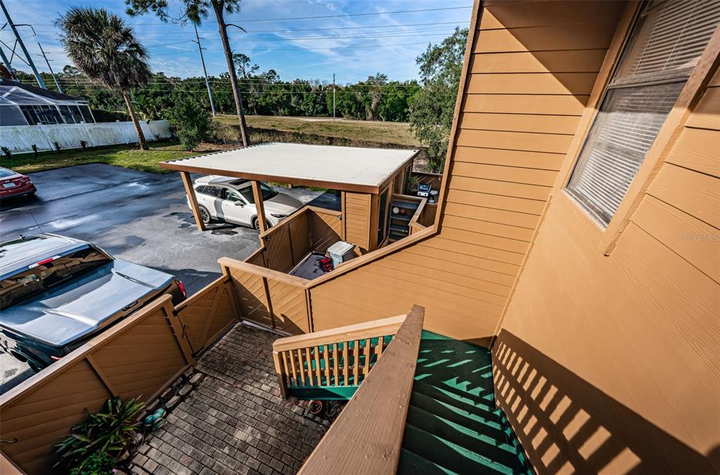 An elevated view of a wooden staircase leading down to a paved patio and carport — 802 LENNOX ROAD W UNIT 802, PALM HARBOR, FL