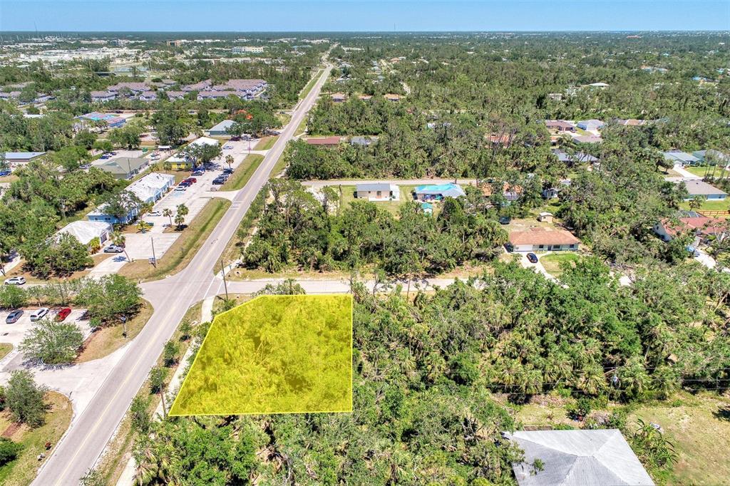 An aerial view shows a vacant, yellow-highlighted lot situated next to a road and trees — 17919 TOLEDO BLADE BOULEVARD, PORT CHARLOTTE, FL