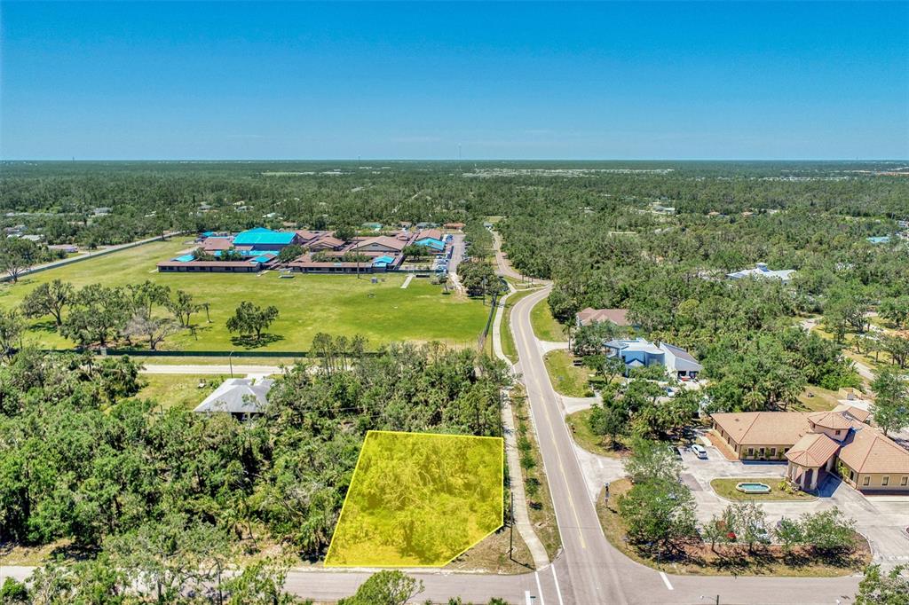 An aerial view shows a vacant, wooded lot highlighted in yellow next to a paved road — 17919 TOLEDO BLADE BOULEVARD, PORT CHARLOTTE, FL