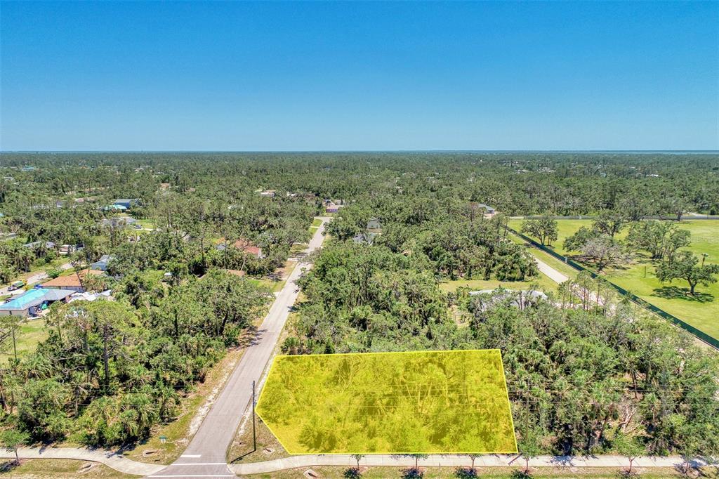 An aerial view shows a vacant, wooded lot highlighted in yellow next to a paved road — 17919 TOLEDO BLADE BOULEVARD, PORT CHARLOTTE, FL