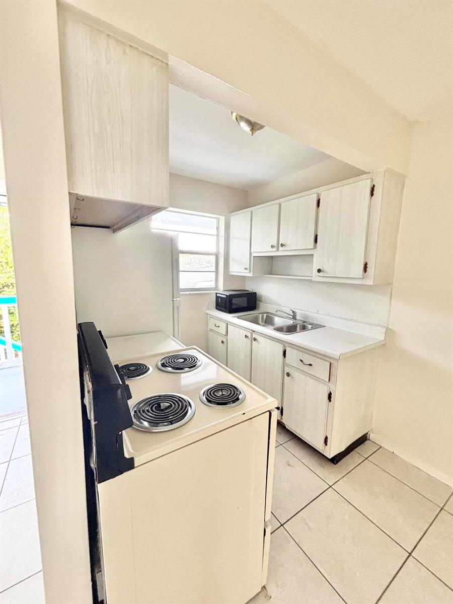 A small kitchen features white cabinets, a white electric stove, and a double-basin sink — 1111 N Federal Highway # 5, FL 33460, FL