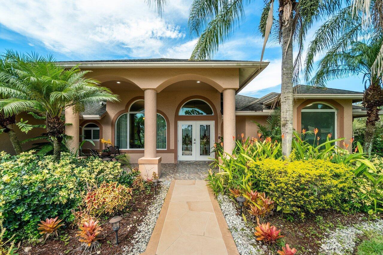 A tan house with a stone walkway, arched entryway, and lush tropical landscaping — 1265 Longlea Terrace, Wellington FL 33414, WELLINGTON, FL
