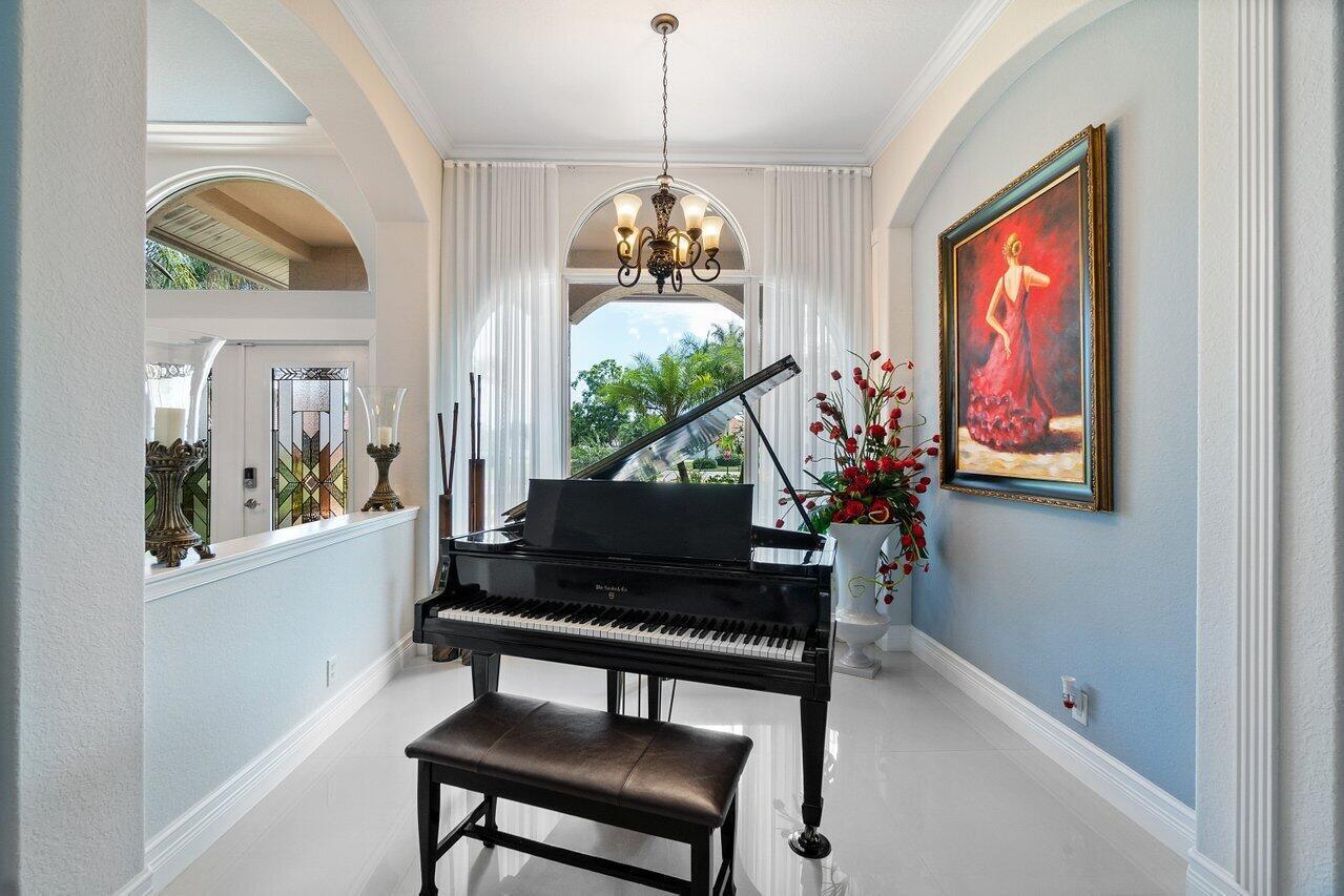 A black grand piano sits in a light blue foyer beneath a chandelier and arched window — 1265 Longlea Terrace, Wellington FL 33414, WELLINGTON, FL