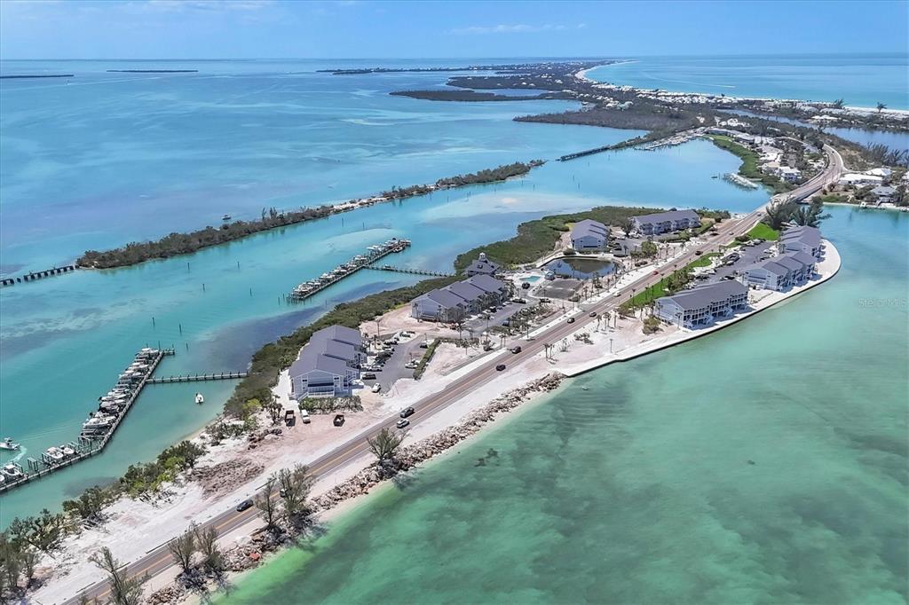 An aerial view shows a narrow coastal road lined with multi-story buildings and boat docks — 6010 BOCA GRANDE CAUSEWAY UNIT C26, BOCA GRANDE, FL