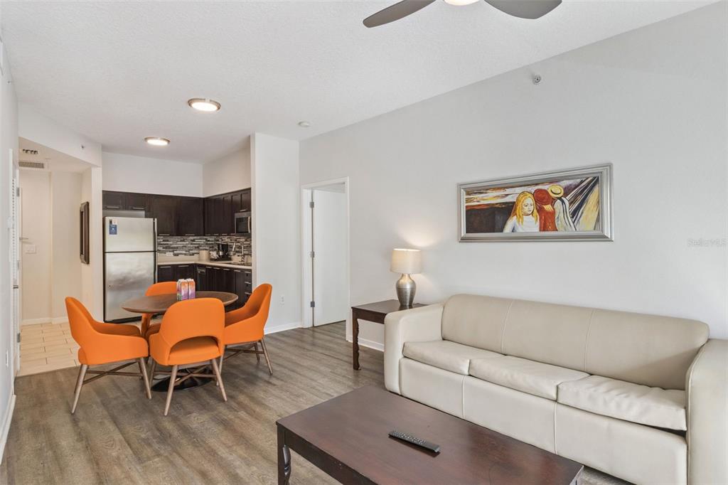 A living room and dining area with wood-look flooring, a beige sofa, and orange chairs — 225 CELEBRATION PLACE UNIT 216, CELEBRATION, FL