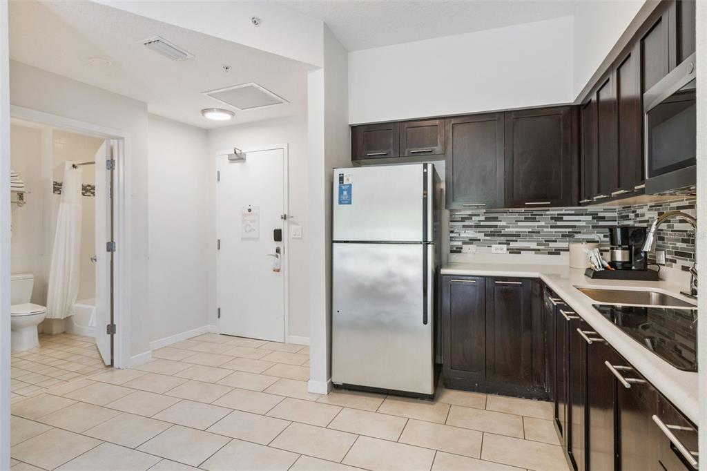 A kitchen with dark wood cabinets, stainless steel appliances, and tile flooring next to a bathroom — 225 CELEBRATION PLACE UNIT 216, CELEBRATION, FL